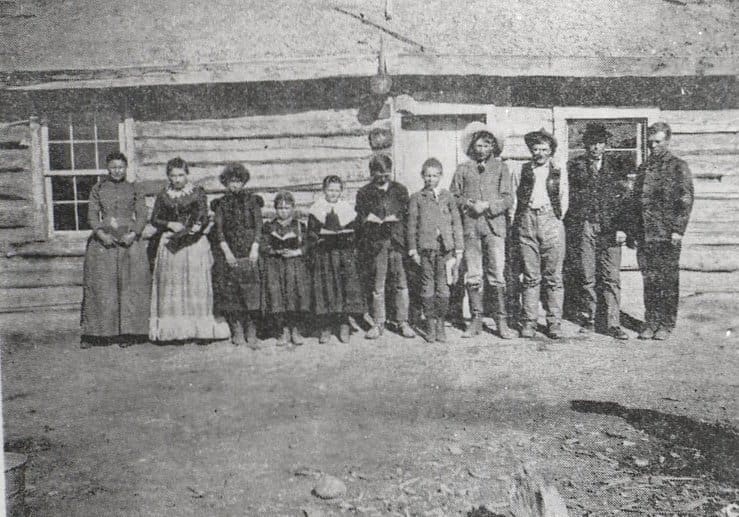 The first school class in Jackson Hole, outside Sylvester Wilson's cabin. Teacher on far right is Henry Johnson, the first schoolteacher in the valley.